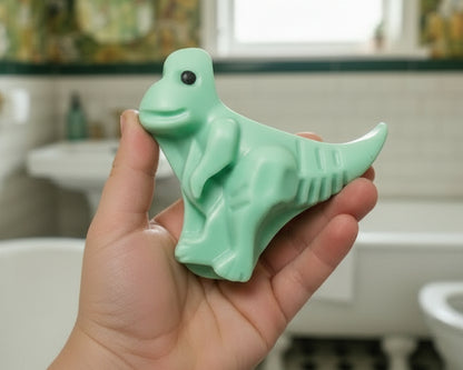 Green dinosaur-shaped object on a beige fabric background with white leaf pattern